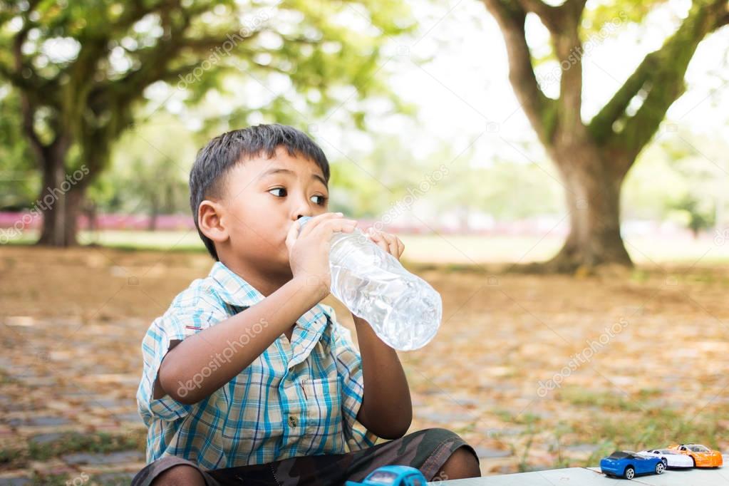 Cute little boy drinking water in the green park,focus hand