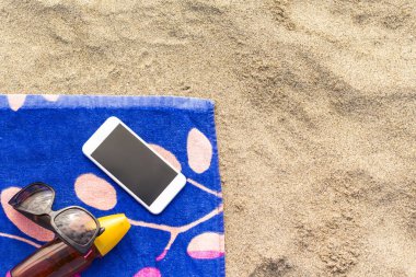 Cep telefonu ile bir plaj havlusu üzerinde güneş koruyucu bir şişe