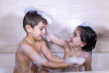 Küvette köpükle oynayan iki çocuk.