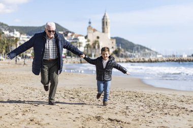 Grandparent with his grandson running on the beach of Sitges, Sp clipart