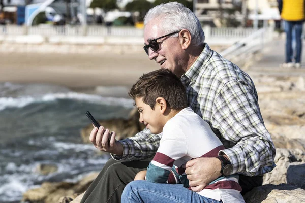 Avô e neto com um celular perto do mar — Fotografia de Stock