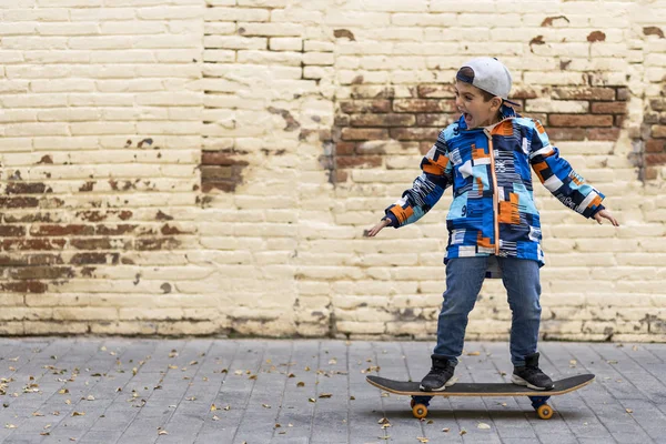 Bonito criança skate embarque com um fundo de parede de tijolo — Fotografia de Stock