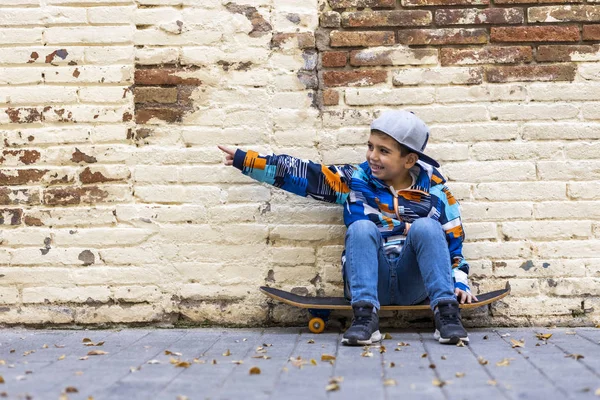 Schattig klein kind zitten op zijn skateboard met een bakstenen muur terug — Stockfoto