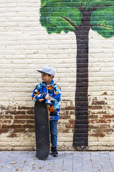 Schattig klein kind zitten op zijn skateboard met een bakstenen muur terug — Stockfoto