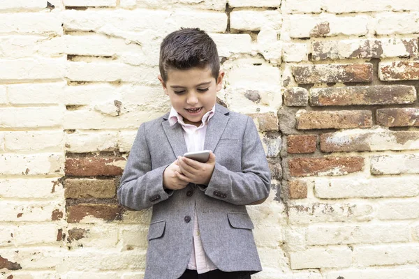 Moda mały dzieciak z telefonem komórkowym na tle cegły ściany — Zdjęcie stockowe