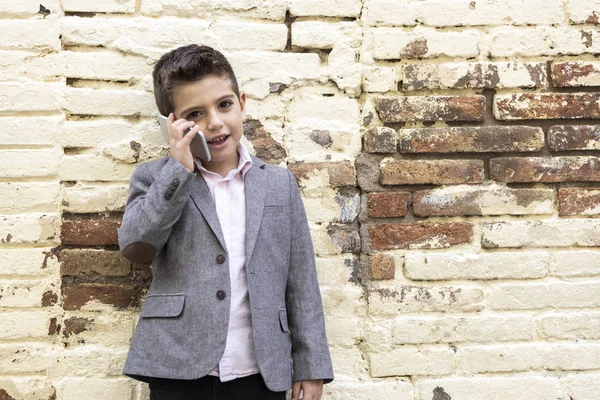 Moda mały dzieciak z telefonem komórkowym na tle cegły ściany — Zdjęcie stockowe