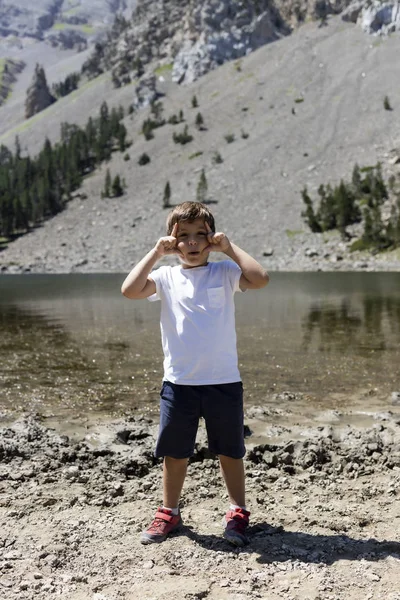 Klein kind maakt een grappig gebaar op een bergmeer — Stockfoto
