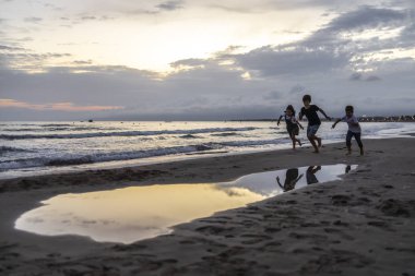 Gün batımında plajda koşan üç çocuk.