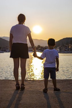 Anne ve oğul gün batımında el ele tutuşuyorlar.