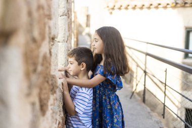 Two kids looking throw the wall of a castle