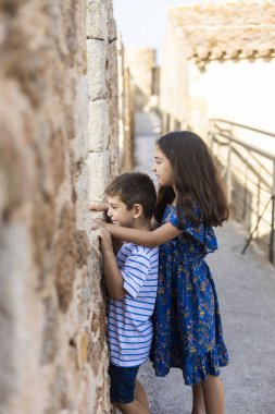 Two kids looking throw the wall of a castle