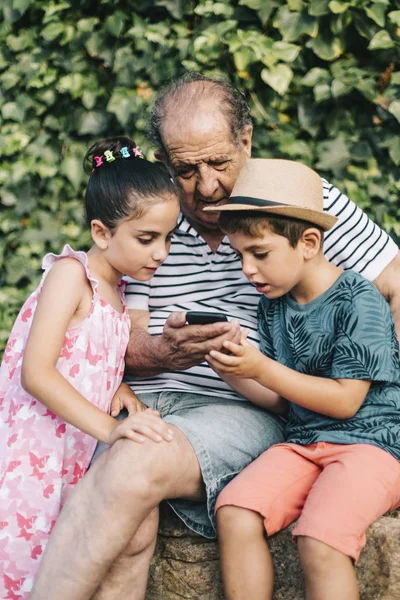 Abuelo y nietos jugando con un teléfono móvil — Foto de Stock