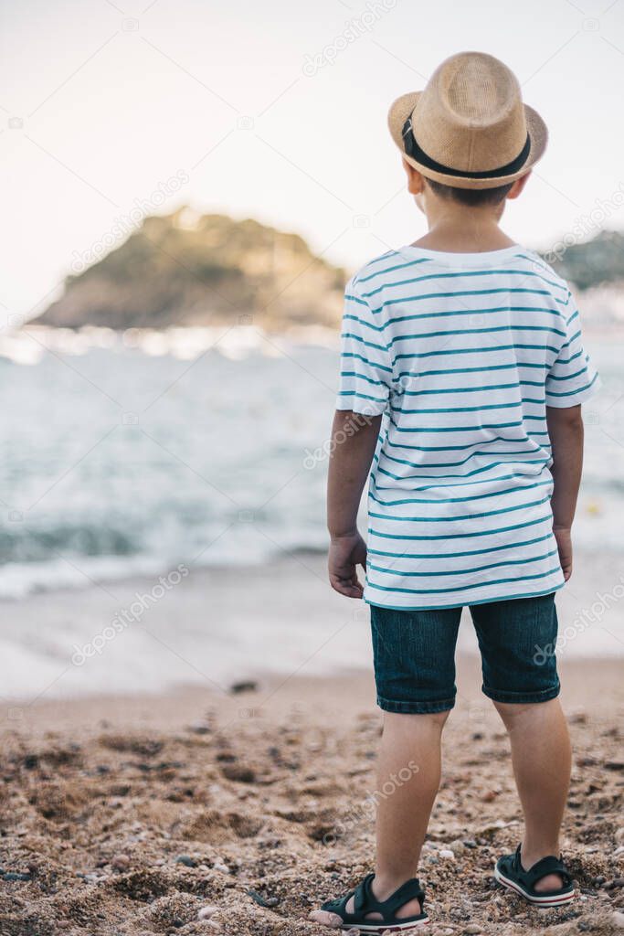 Little kid with hat looking the sea on the beach
