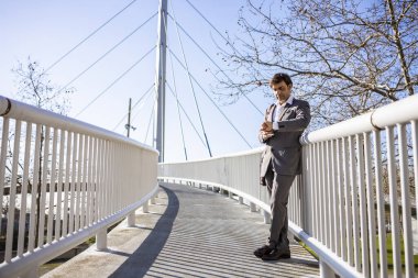 Orta yaşlı işadamı elinde kahveyle köprüde bekliyor.