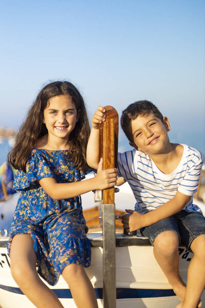 Портрет двух маленьких детей, забравшихся на рыбацкую лодку на пляже
