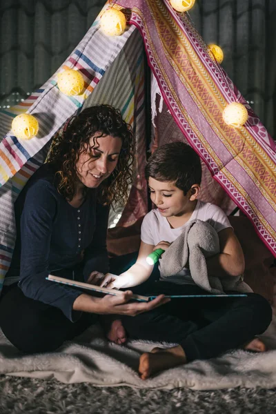 Mother and son reading a book on a tent at home