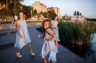 Anne ve iki kız gün batımında göletin yanında yürüyorlar. Odaklanan bir kız.
