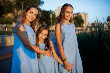 Anne ve iki kız gün batımında göletin kenarında yürüyorlar.