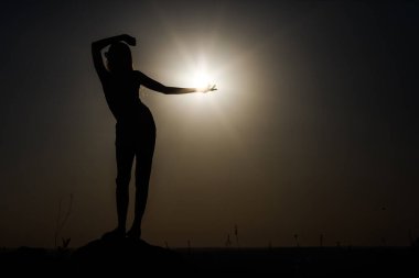 Gün batımında yükselen bir kızın silueti. Güneşi tutmak gibi..