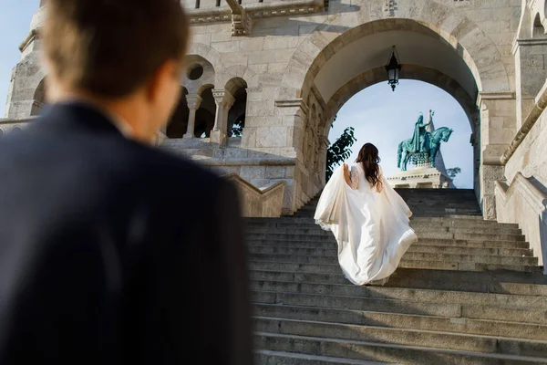 Couple. The bride stands with her back turned and looks at the sky. The groom is partially visible. He out of focus