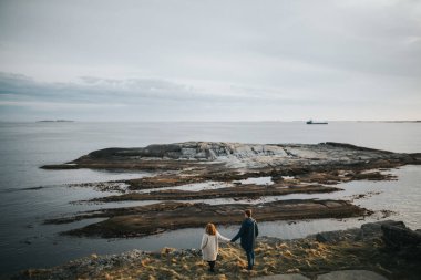 Norveç. Çift el ele tutuşup manzarayı izliyor. Gün batımı.