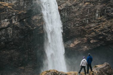 Norveç. Çift el ele tutuşup manzarayı izliyor. Gün batımı. Şelale.