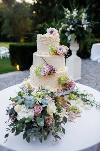Wedding cake standing on the table. Around the flowers. Outside