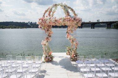Gölün arka planında bir düğün töreni için çiçeklerle kaplı kemer. Güzel çiçeklerle kurulmuş bir düğün, açık havada.