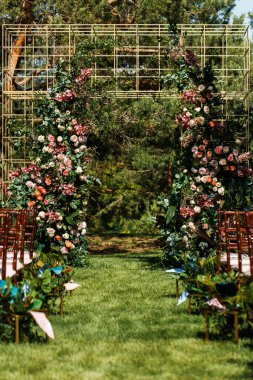Tören için dışarıda çimlerin üzerinde düğün kemeri. Misafirler için görünür sandalyeler. Bir sürü çiçek..