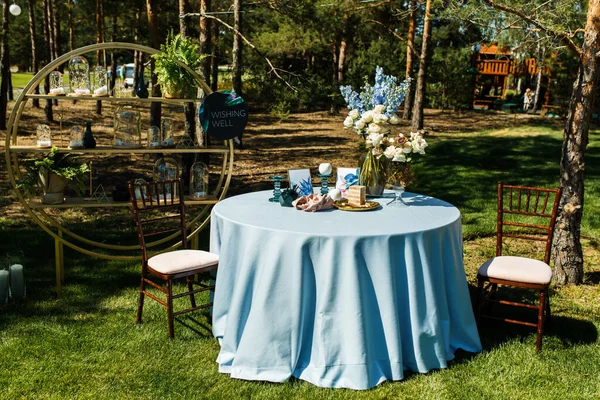 The guest table is decorated with flowers. On the side there is a round rack decorated with glass flasks and greenery.