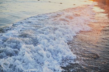 Deniz kıyısı. Gün batımı. Dalgalar vurur ve su köpükleri.