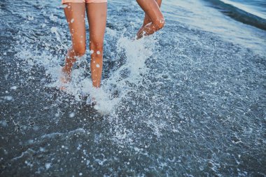 Kızlar denizin kenarında dururlar. Gün batımı.