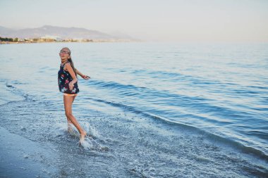 Kız sahil boyunca yürür. Gün batımı. Poz veriyor. Suda akıyor..