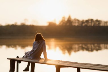 Kız ormanda suyun yanında vakit geçirir. Hırka giyiyorlardı. İyi eğlenceler ve gün batımını izleyin. Siluet.