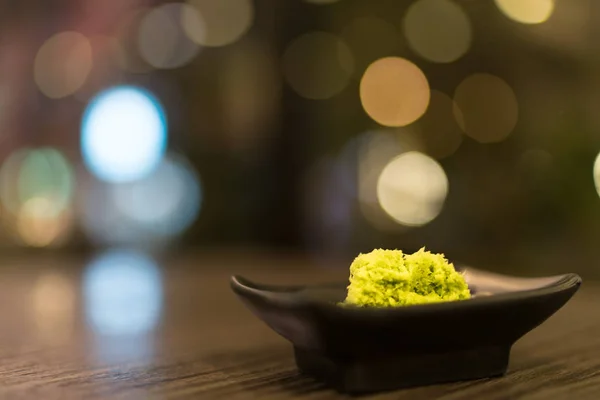 Wasabi in black saucer on wooden table with depth of field effect, Japanese food's condiment, bokeh background — Stock Photo, Image