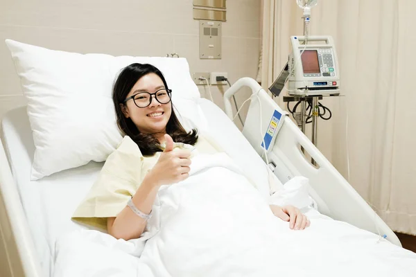 Asiatique patient fille pouces vers le haut ok signe et sourire tout en se reposant sur lit d'hôpital, concept médical positif — Photo
