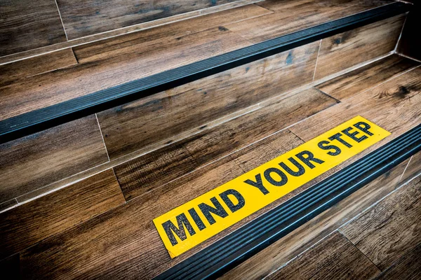 Mind your step sticker sign pasted on wooden stair. Warnings, abstract, or indoor architecture concept — Stock Photo, Image