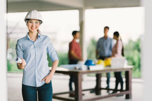 Female architect or engineer with blueprint at building construction site. Coworker meeting on blur background. Industry, teamwork discussion, or job occupation concept