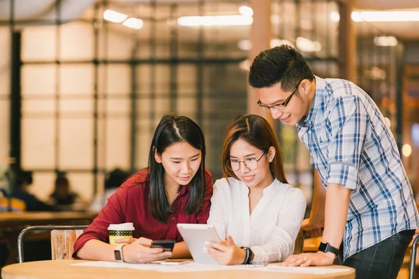 Jóvenes estudiantes universitarios asiáticos o compañeros de trabajo que utilizan tabletas digitales y teléfonos inteligentes juntos en la cafetería, grupo diverso. Negocios casuales, trabajo independiente en la cafetería, reunión social o concepto de educación — Foto de Stock