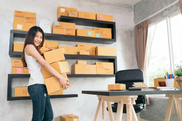 Young Asian small business owner carrying product boxes at home office, online marketing packaging and delivery scene, startup SME entrepreneur or freelance woman working at home concept — Stock Photo, Image