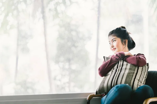 Beautiful young Asian girl relaxing at home, sitting alone by window, looking at copy space. Concept of lonely woman, thinking, or missing someone. — Stock Photo, Image
