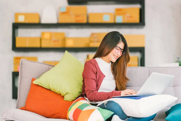 Joven dueño de una pequeña empresa asiática que trabaja en el ordenador portátil en casa, embalaje de marketing en línea y la escena de la entrega, emprendedor PYME startup o concepto de mujer independiente — Foto de Stock