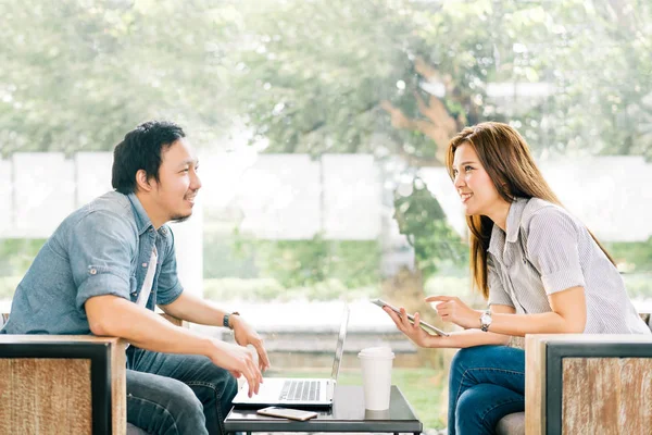 Joven pareja asiática o compañero de trabajo hablando en la cafetería u oficina moderna, fondo de jardín. Con portátil portátil, smartphone y tableta digital. Estilo de vida moderno con concepto de tecnología de gadget de computadora — Foto de Stock