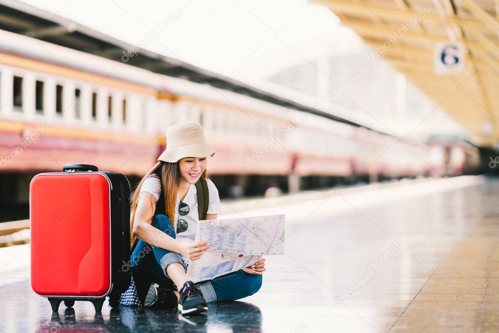 Asian backpack traveler woman using generic local map, siting alone at train station platform with luggage. Summer holiday traveling or young tourist concept