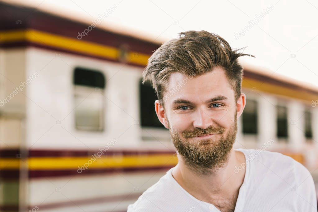 Portrait of smiling handsome European man standing at public train station. Happy backpack traveler or holiday vacation tourism concept