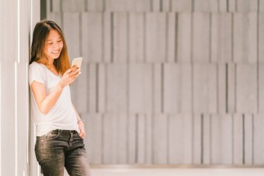 Smartphone kullanarak ve gülümseyen genç güzel Asyalı kız ya da üniversite öğrencisi. Modern yaşam tarzı, mobil iletişim teknolojisi, gündelik iş veya eğitim kavramı