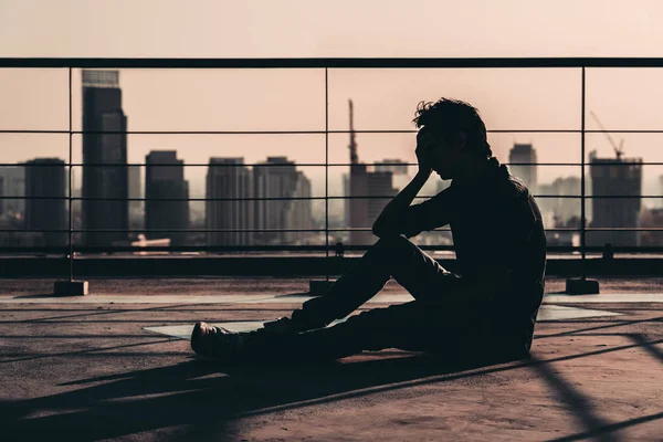 Silhouette of sad depressed Asian man lost hope and cry, sit on building rooftop at sunset, dark mood tone. Concept of major depressive disorder, friend zone, unemployment, stress emotion or paranoid — Stock Photo, Image