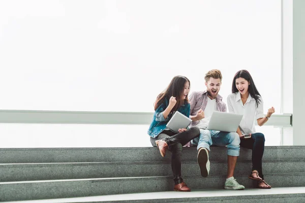 Grupo multiétnico de estudiantes universitarios o compañeros de trabajo independientes celebran junto con el ordenador portátil y la tableta. Equipo creativo o colega de negocios en la oficina moderna. Startup, trabajo en equipo, concepto de proyecto de éxito — Foto de Stock