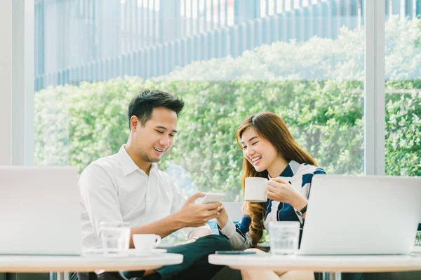 Unga asiatiska par, medarbetare eller affärspartner har kul med smartphone tillsammans med bärbar dator på coffee shop. Informationsteknik, café livsstil eller romantisk relation koncept — Stockfoto