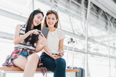 İki mutlu Asyalı kız akıllı telefon kontrol uçuşu kullanıyor ya da havaalanında bavullarıyla birlikte kayıt yaptırıyor. Hava yolculuğu, yaz tatili veya cep telefonu uygulama teknolojisi konsepti